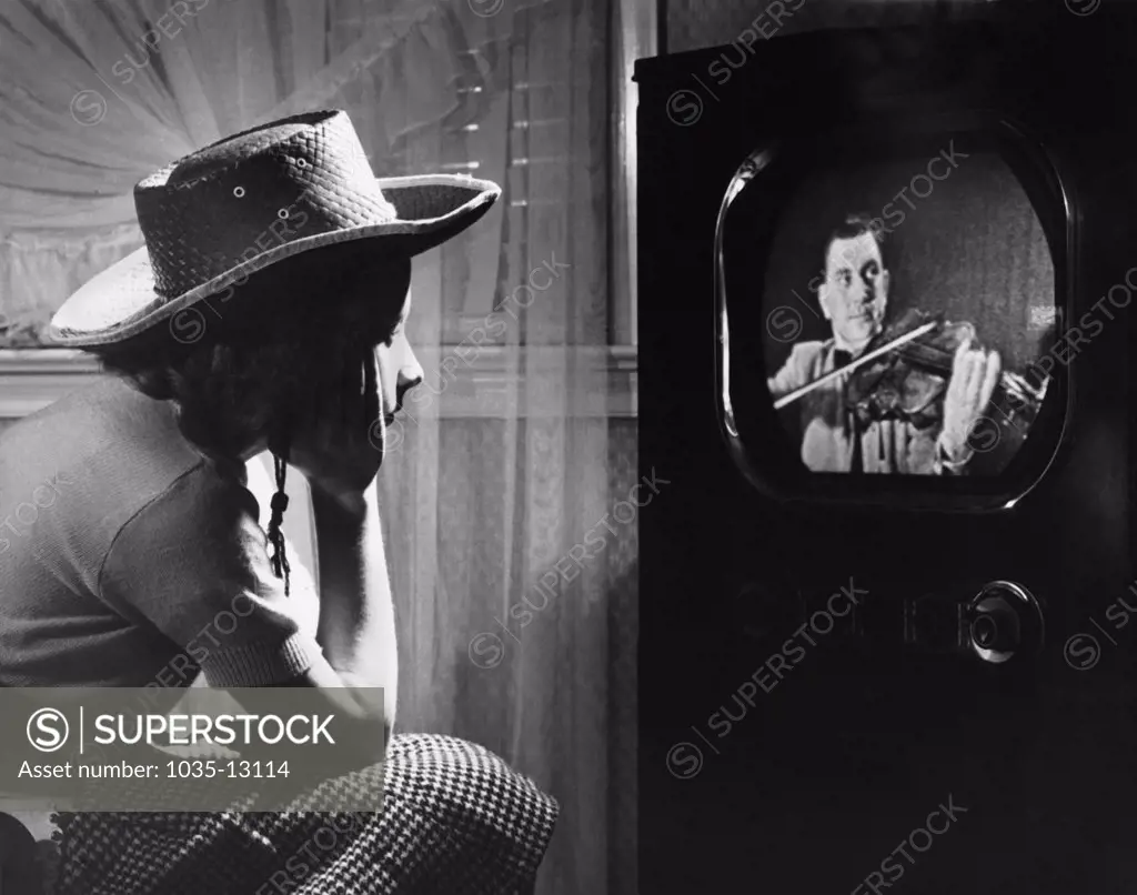 United States:  c. 1954 A young girl wearing a cowboy hat watching a man play violin on television.