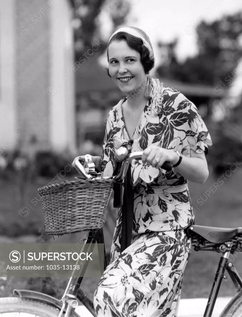 United States:  c. 1928 A smiling woman on her bicycle.