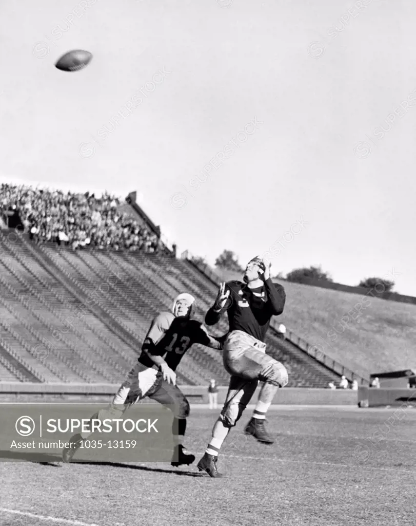 Berkeley, California:  c. 1936 A football player runs down field to catch a pass with the defender close by.