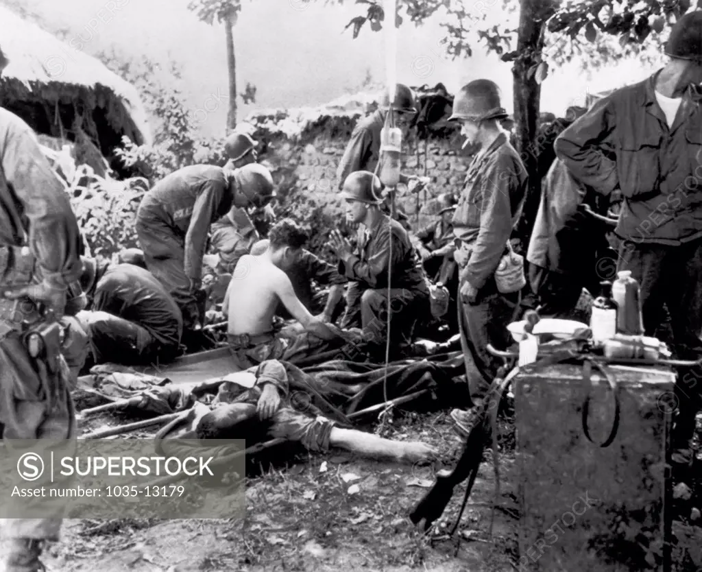 Korea:  August 10, 1950 A U.S. Army chaplain prays while wounded soldiers get dressings and plasma at a medical station on the war front.