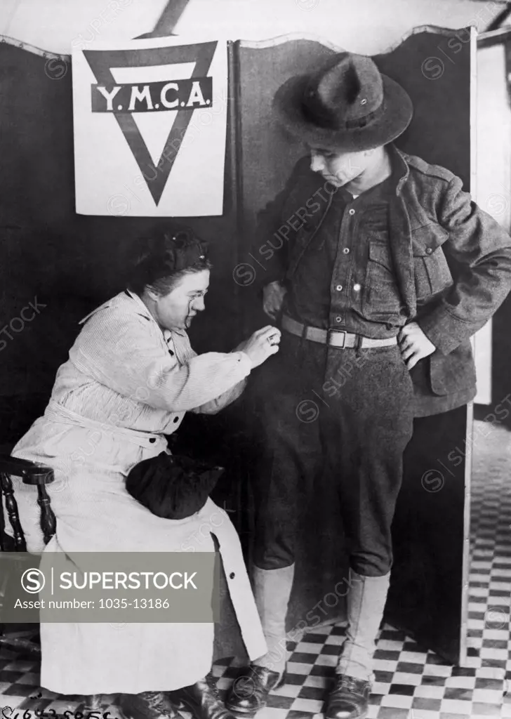 London, England:  c. 1917 A soldier gets some last minute repairs made to his uniform by a woman at the YMCA in London.