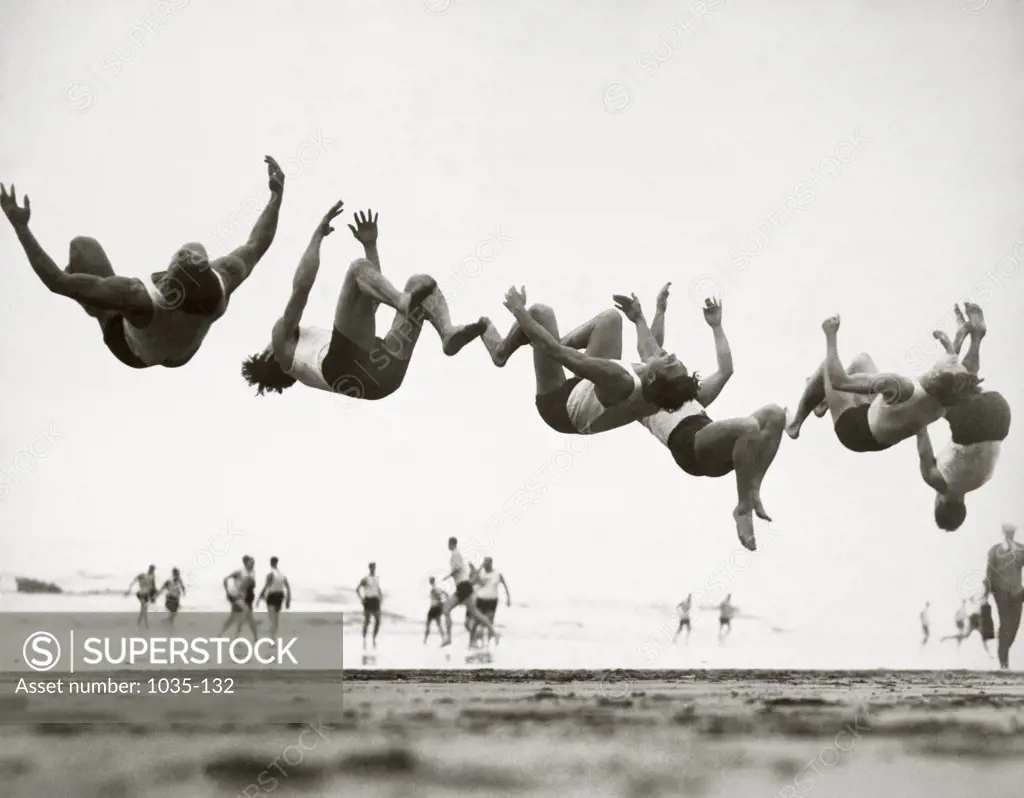 Group of teenage boys performing back flip on the beach