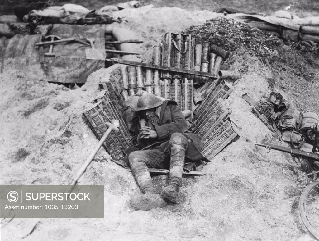Europe: c. 1917 An exhausted soldier in WWI curls up to sleep using captured German ammunition for a mattress