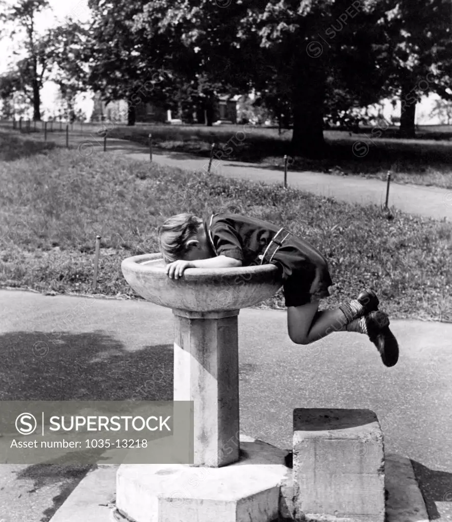 United States:  c. 1932 A enterprising young boy gets a drink of water from a fountain.