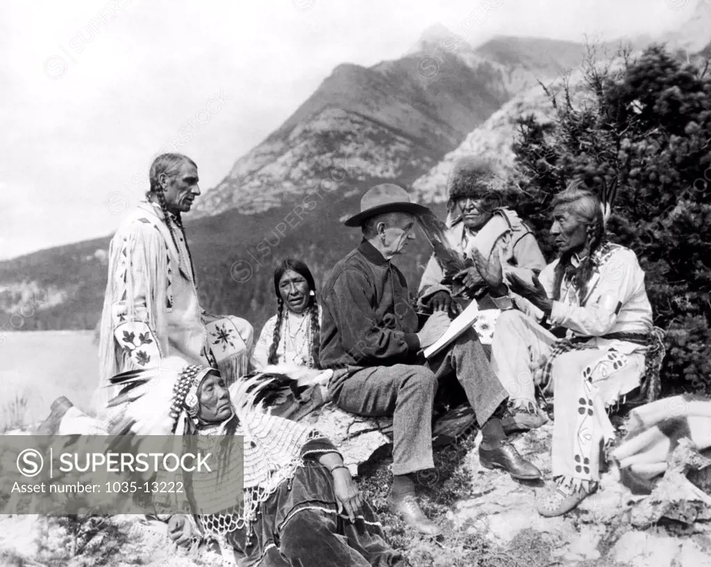 Montana: c. 1927. Author James Willard Schultz amongst Blood Indians of the Blackfoot Tribes. He is using the universal sign language of the Native Americans to translate their legends and stories.