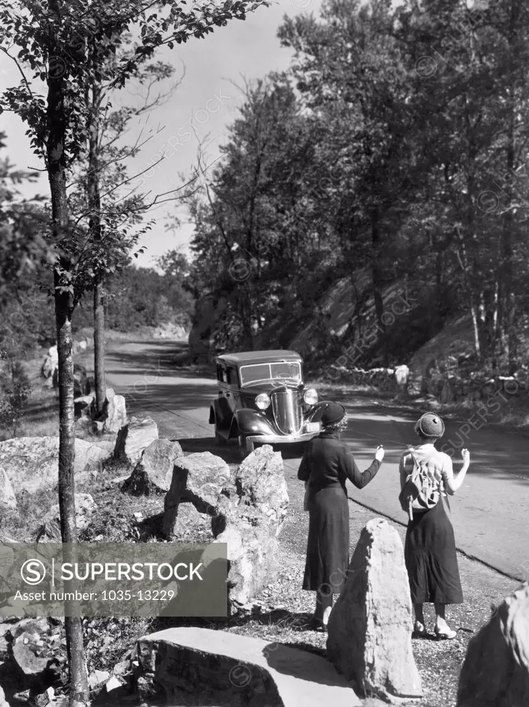 United States:  c. 1927 A car pulls over to pick up two young women hitchhiking on a country road.