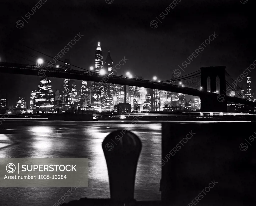 New York, New York:  c. 1938 A nighttime view of the Brooklyn Bridge with the New York City skyline behind it.