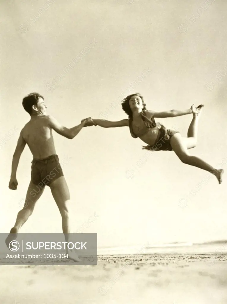 Rear view of a young man supporting a young woman jumping in the air