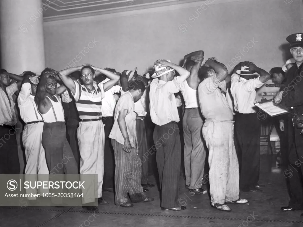 Detroit, Michigan:  June 24, 1943 Blacks under arrest being booked into jail by a white police officer in the aftermath of the three days of riots over wartime housing.