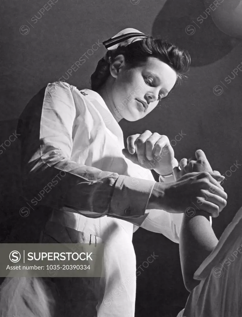 United States:  January, 1944 A U.S. Navy nurse on duty with the U.S. Marine Corps Women's Reserve checking the pulse on a patient.