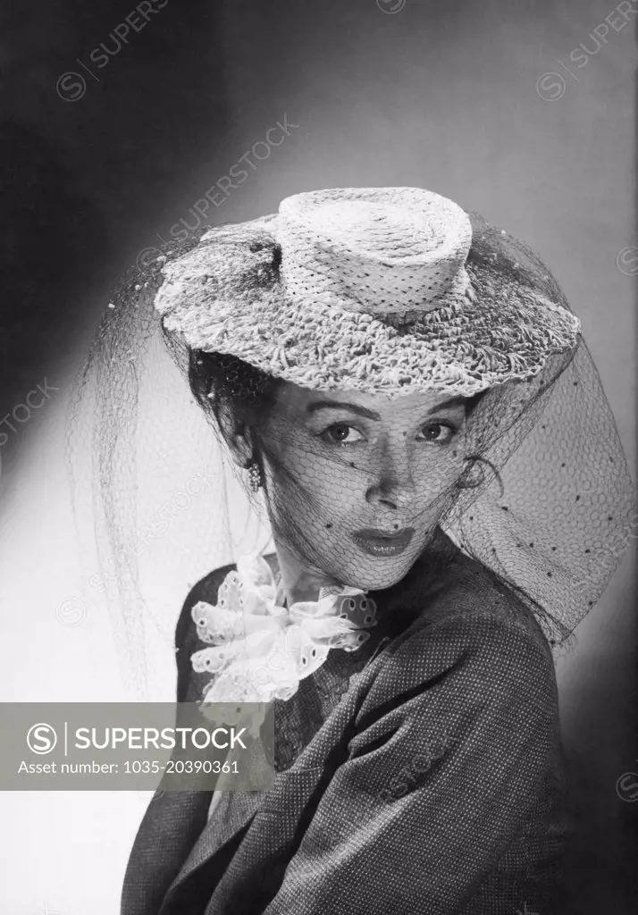 United States:  c.  1948 A fashion photo of a woman wearing a hat with a veil.