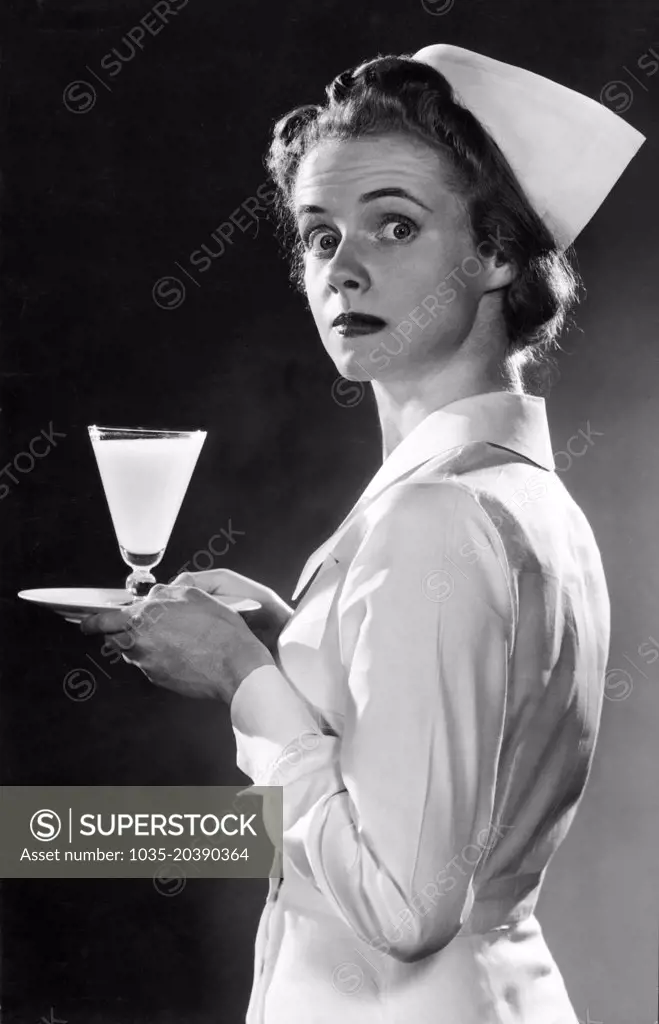 United States:  c.  1947 A nurse looking surprised as she is photographed carrying a glass of milk on a tray.