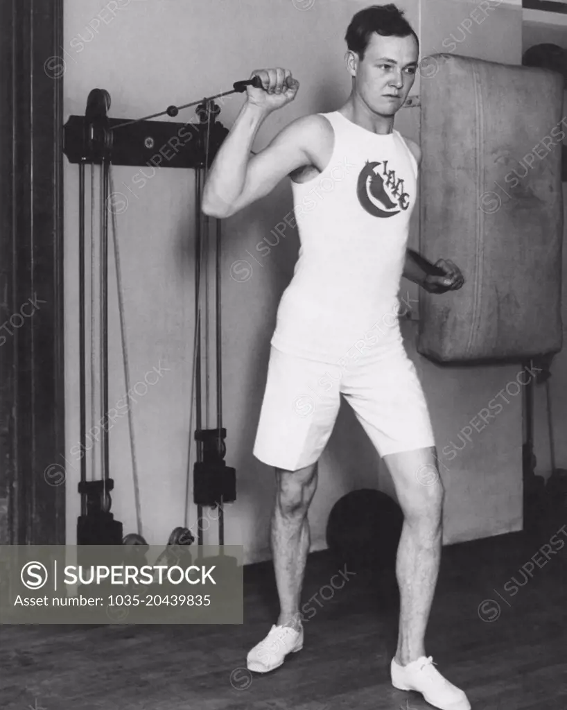 United States:  c. 1923 A man exercising with a weight machine.