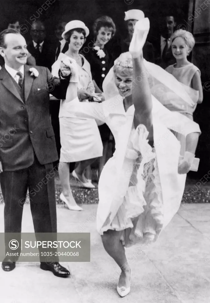 London, England:  August 20, 1961 Showgirl Margaret Cooper holds her new husband's hand as she executes a joyful high kick following their wedding.