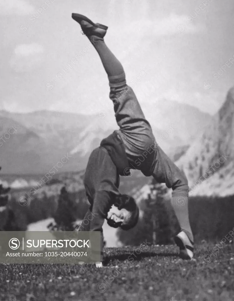 Bow Valley, Alberta, Canada:  August 9, 1923 A limber young woman does a hand stand with the splits in a meadow in the Canadian Rockies.
