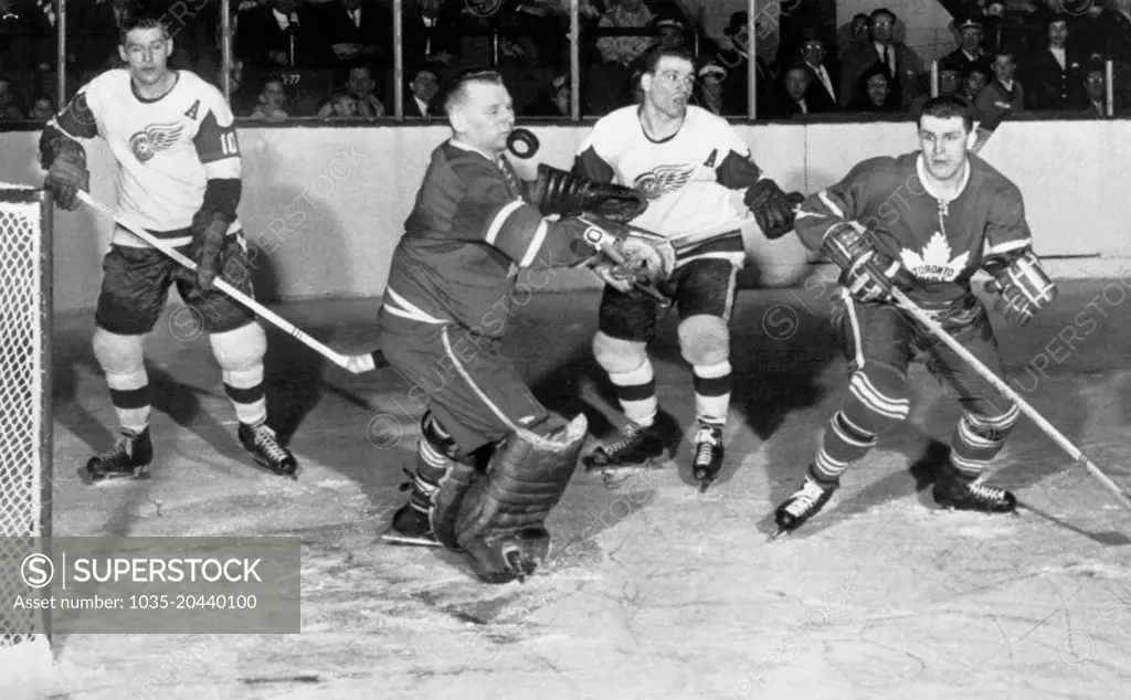 Toronto, Canada:   February 5, 1961 Toronto Maple Leaf goalie Johny Bower appears to be stopping the puck with his chin in a National Hockey League game against the Detroit Red Wings. Toronto won, 4-2, to take ove first place.