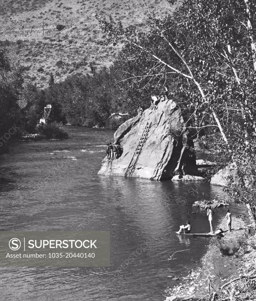 United States:  1910 Boys diving off a huge rock at the swimming hole in the river.