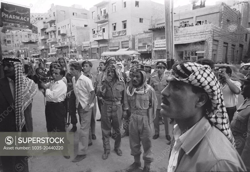 Amman, Jordan:  July, 1958 Men and soldiers gathered on a street intently watching something in a storefront window, possibly news reports of the overthrow of King Faissal by Saddam Hussein  in neighboring Iraq.