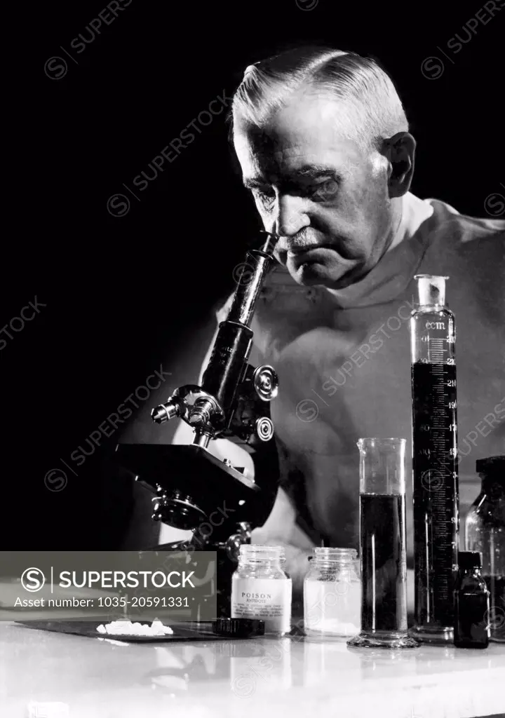 United States:  c.  1940 A scientist looking at a poison antidote through a microscope.