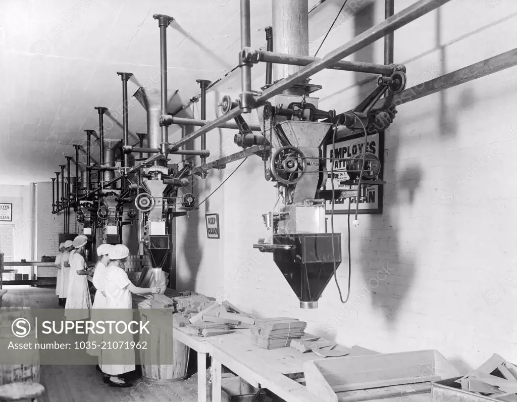 United States:  c. 1913 Women employees using Scott filling machines in a factory.