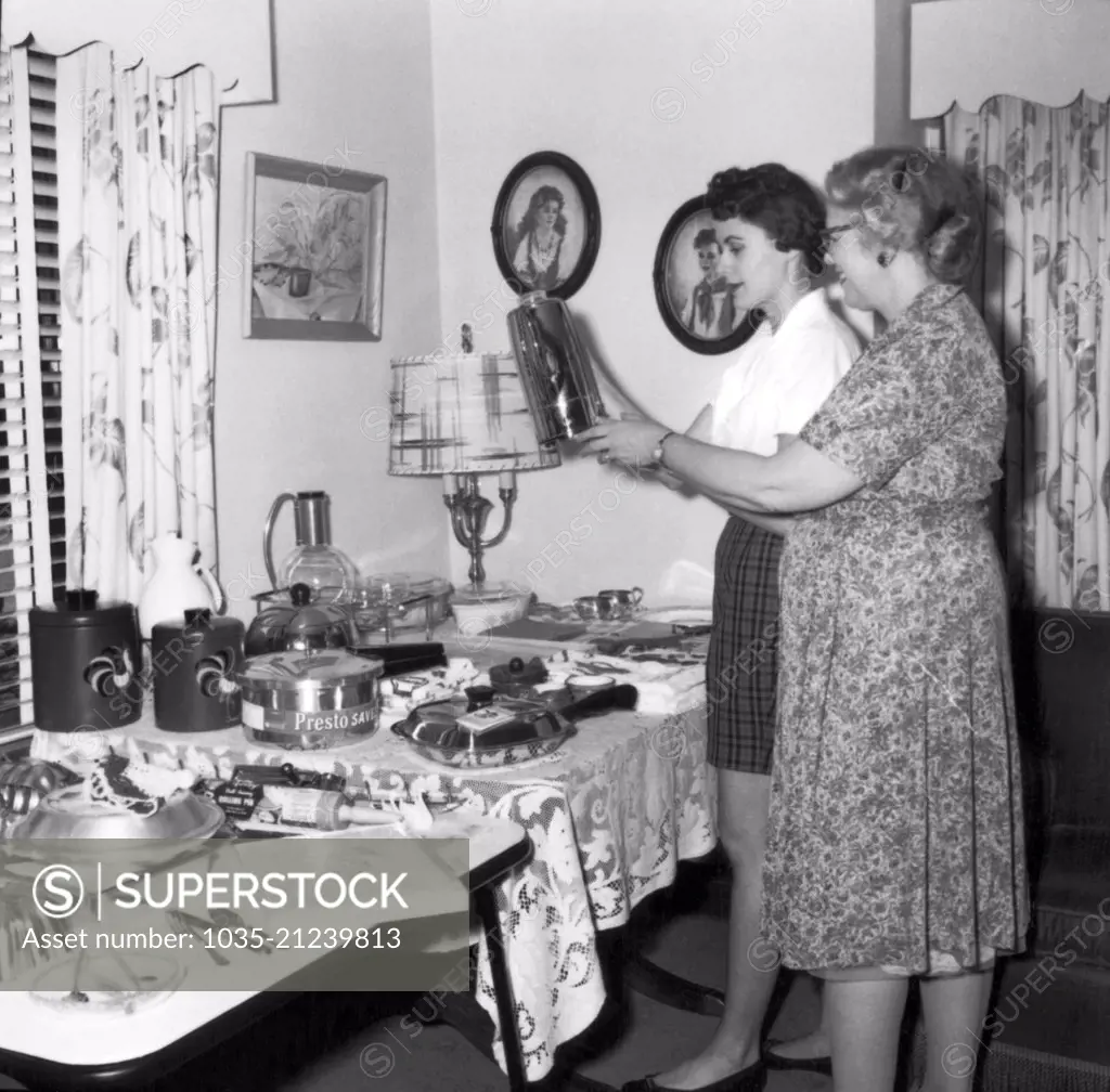 United States:  c. 1961 Two women at a housewares party look at a coffe pot.