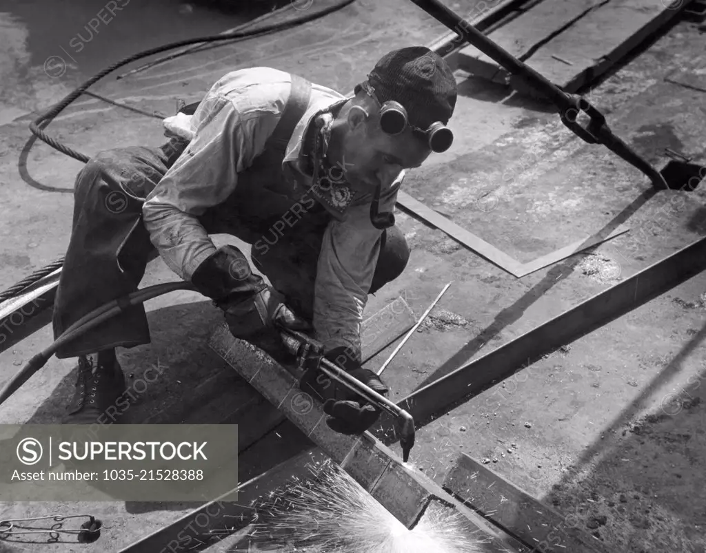 United States:  c. 1938 A workman using an oxy acetylene torch to cut steel angle iron.