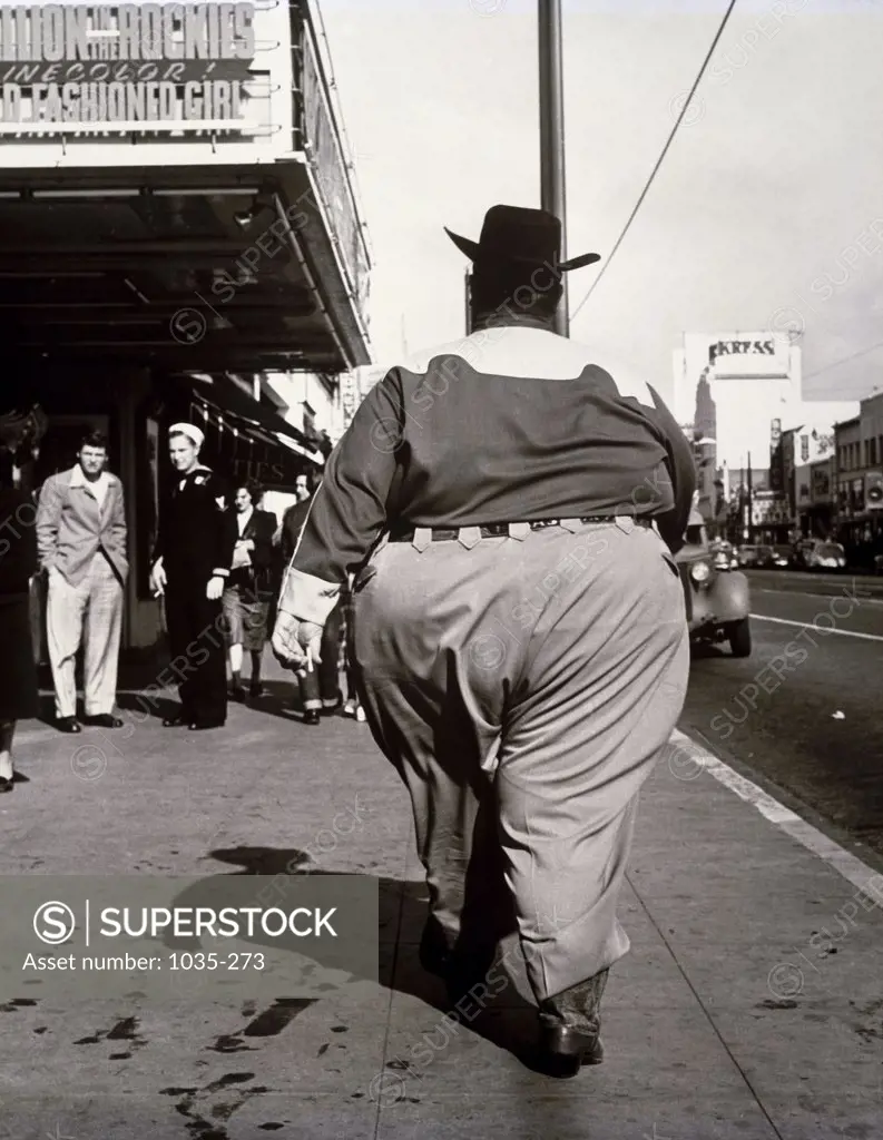 Rear view of an obese man walking on a sidewalk