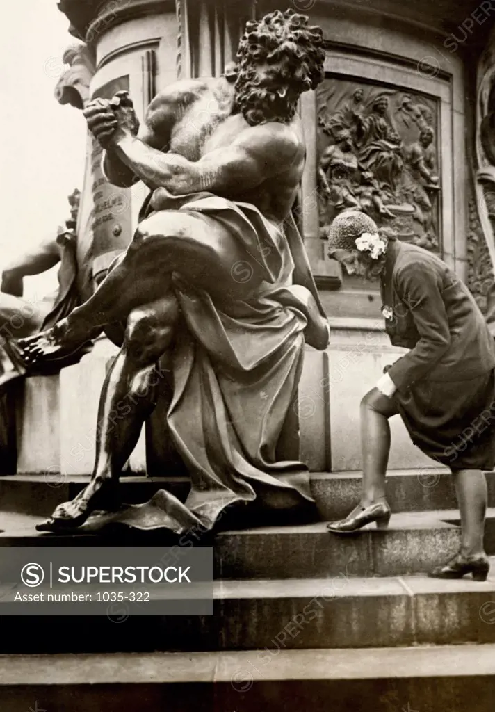 Low angle view of a young woman standing near a statue adjusting her stocking, Berlin, Germany