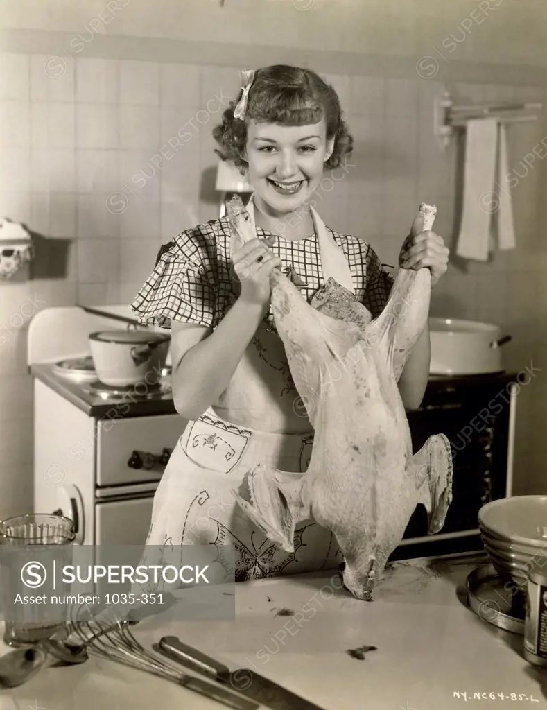 Portrait of a young woman standing in the kitchen and holding a raw turkey