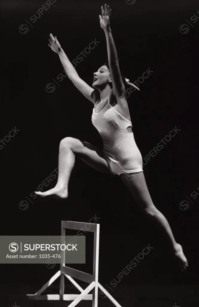 Side profile of a young woman jumping over a hurdle