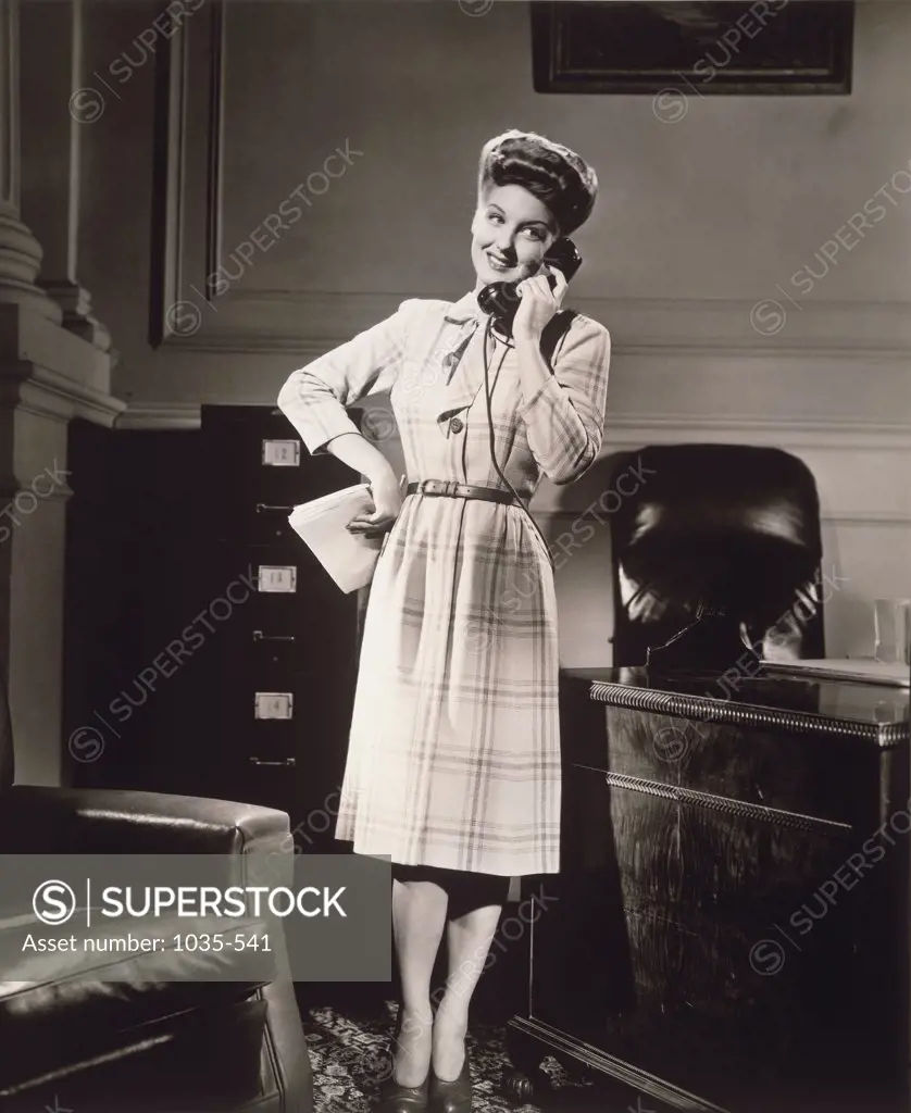 Businesswoman leaning against a desk and talking on a phone