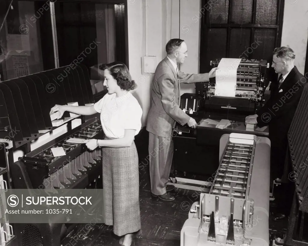 Two businessmen and a businesswoman working on computers in an office, IBM Accounting System, 1951