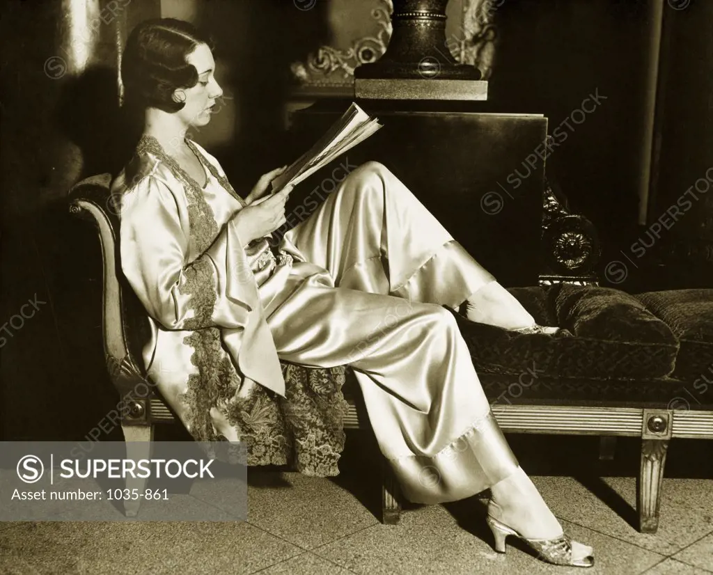 Side profile of a young woman reading a book on chaise lounge