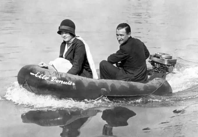 London, England: c. 1931. A happy English couple on an outing on the Thames. They are in a rubber lifesaving boat outfitted with an American outboard motor to push it along.©Underwood Archives