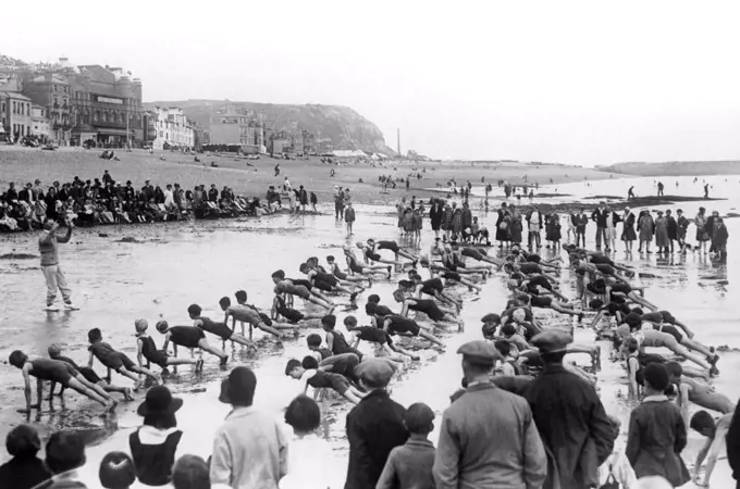 Hastings, England:  c. 1928 A drill instructor gives visiting kids a workout on the beach opposite Caroline Parade.