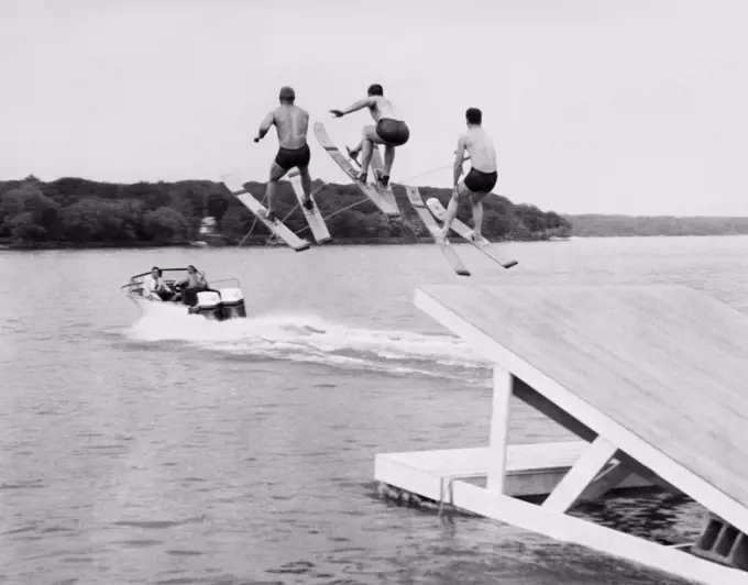 United States:  c. 1956 Three members of the Min-Aqua Bats Waterski Club take the jump simultaneously as part of the water ski show.