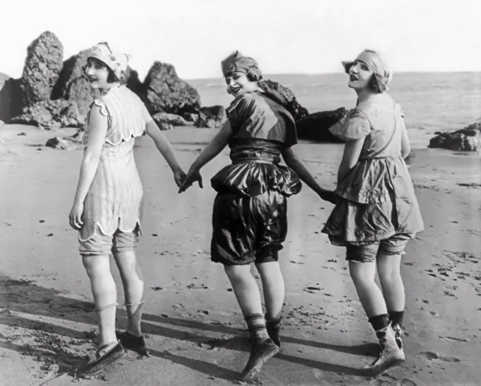Los Angeles, California:  October, 1918 Silent film actresses Lillian Langston, Edith Roberts, and Myrtle Reeves, laughlingly pose holding hands on the beach.