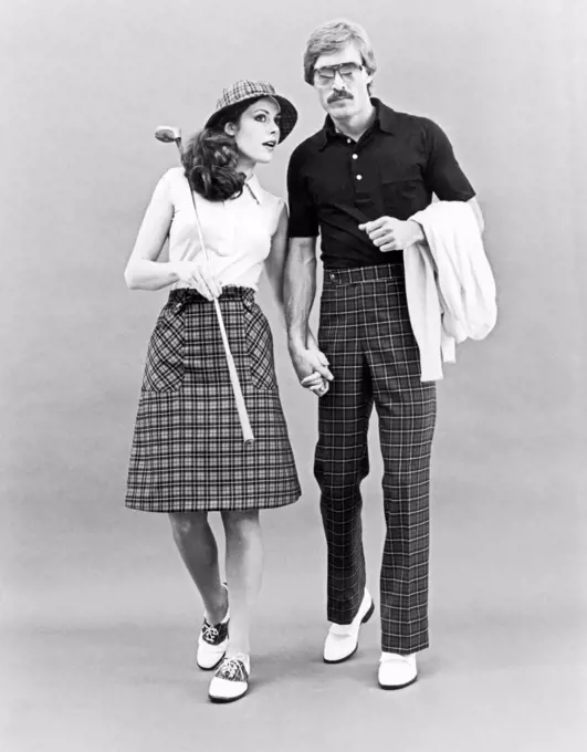 United States:  c. 1962 A stylish couple in checkered golf attire holding hands. She's wearing saddle shoes and he has white tasseled loafers.