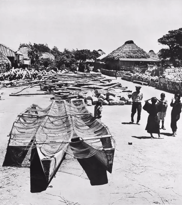 Okinawa, Japan:  May 21, 1945 A village on Okinawa with their fishing boats and nets in the foreground and the rocks and logs that they use to build their homes and huts piled in back.