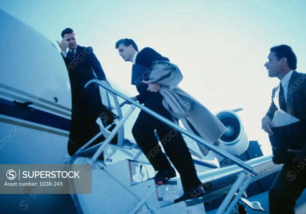 Three businessmen moving up a staircase to an airplane