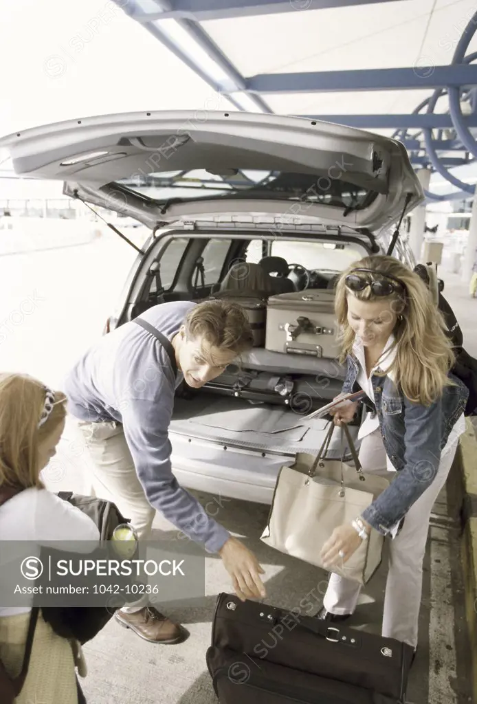 Parents with their daughter standing behind a car with their luggage