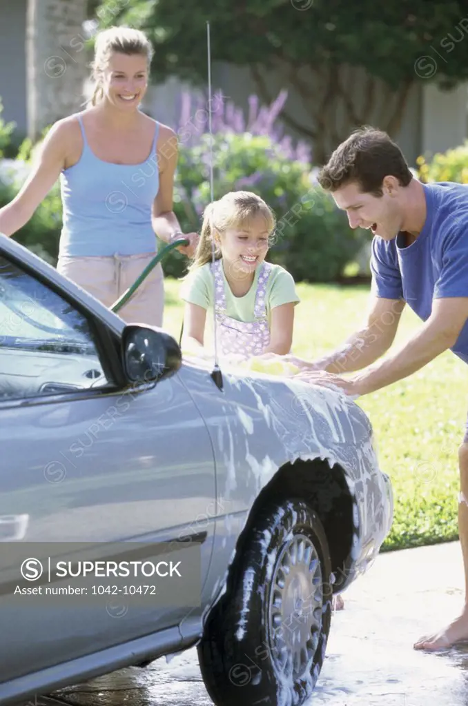 Parents washing the car with their daughter