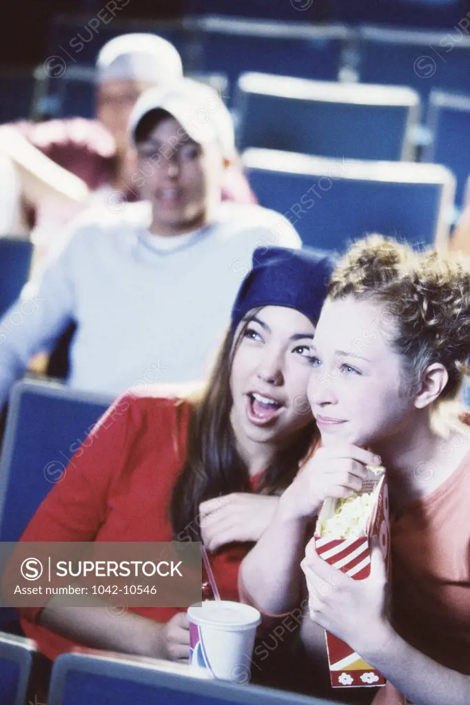 Two teenage girls sitting in a theater watching a movie