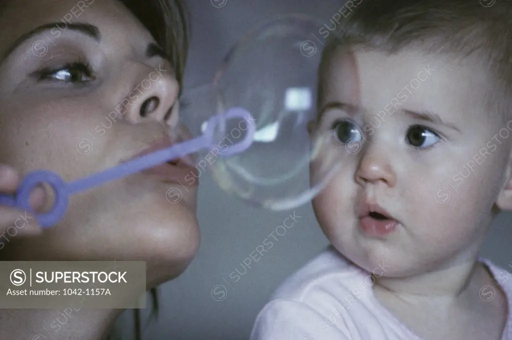 Close-up of a mid adult woman blowing bubbles with a bubble wand and her daughter looking at her