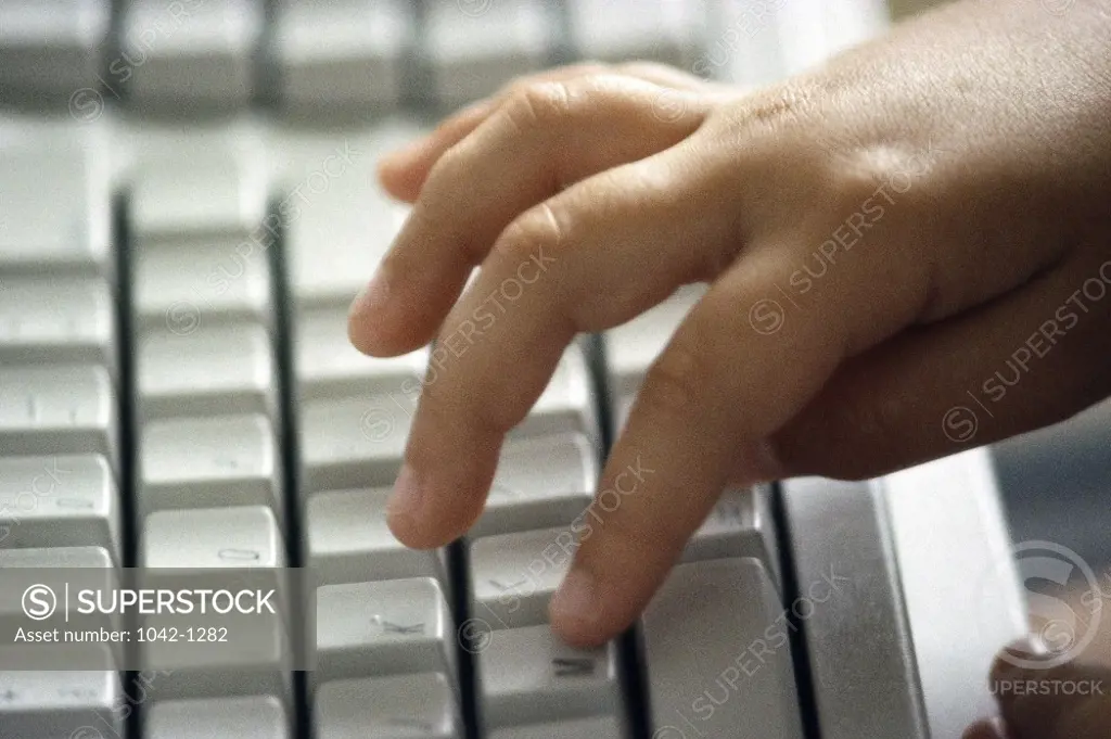 Close-up of a child's hand typing on a computer keyboard