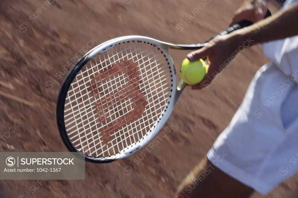 Mid section view of a person's hands holding a tennis racket and a tennis ball