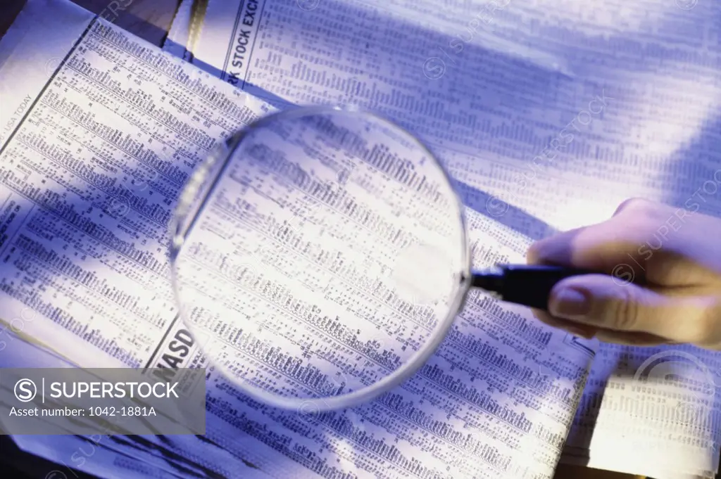 Close-up of a person's hand holding a magnifying glass over a newspaper