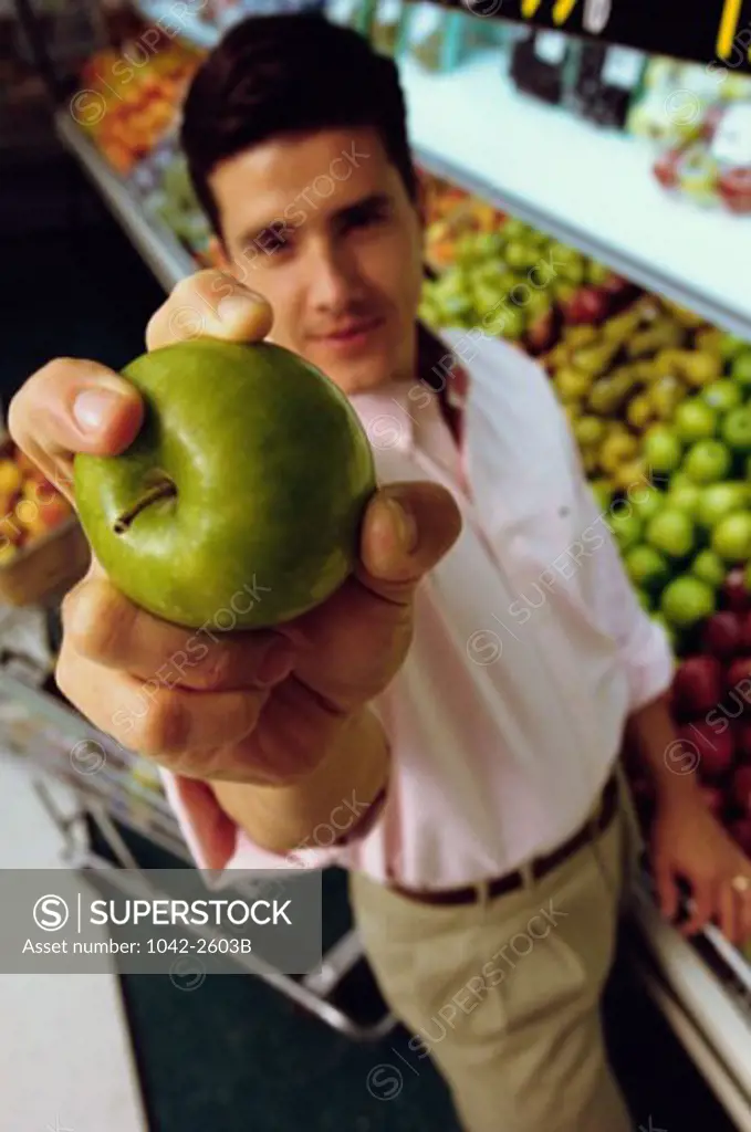 Portrait of a young man holding an apple in a supermarket