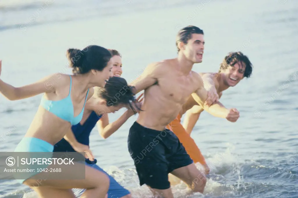 Side profile of a group of young men and women running on the beach