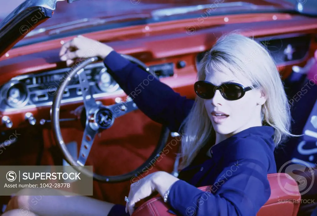 Portrait of a young woman sitting in car holding a steering wheel